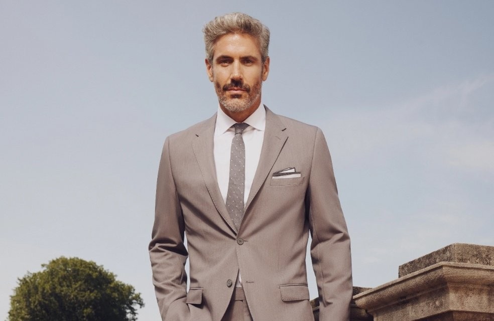 Middle aged man with gray hair wearing perfect fit light grey suit at outdoor wedding venue.